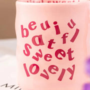 Pink and blue aesthetic wavy ceramic mugs with quirky "beautiful, sweet, lovely" text, held by hands against a neutral background.