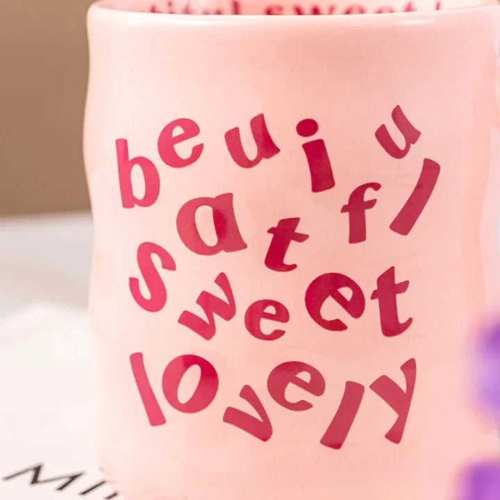 Pink and blue aesthetic wavy ceramic mugs with quirky "beautiful, sweet, lovely" text, held by hands against a neutral background.