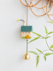 Whimsical wooden house wind chimes with golden bell accents hanging on a rustic frame, perfect for home and garden décor.