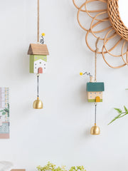 Whimsical wooden house wind chimes with golden bell accents hanging on a rustic frame, perfect for home and garden décor.