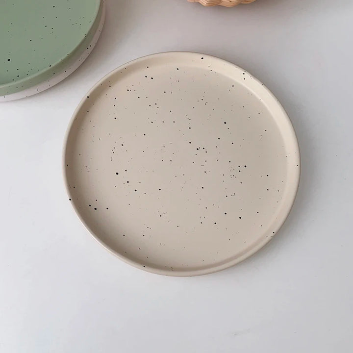 Three minimalist speckled ceramic plates in cream, light grey, and sage green