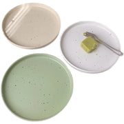 Three minimalist speckled ceramic plates in cream, light grey, and sage green