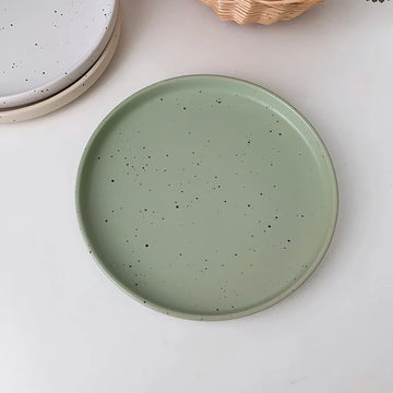 Three minimalist speckled ceramic plates in cream, light grey, and sage green