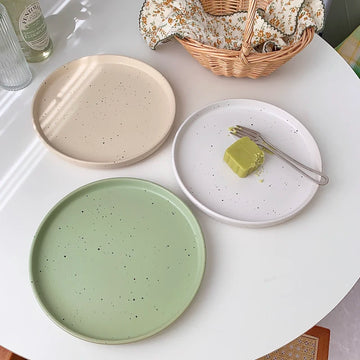 Three minimalist speckled ceramic plates in cream, light grey, and sage green