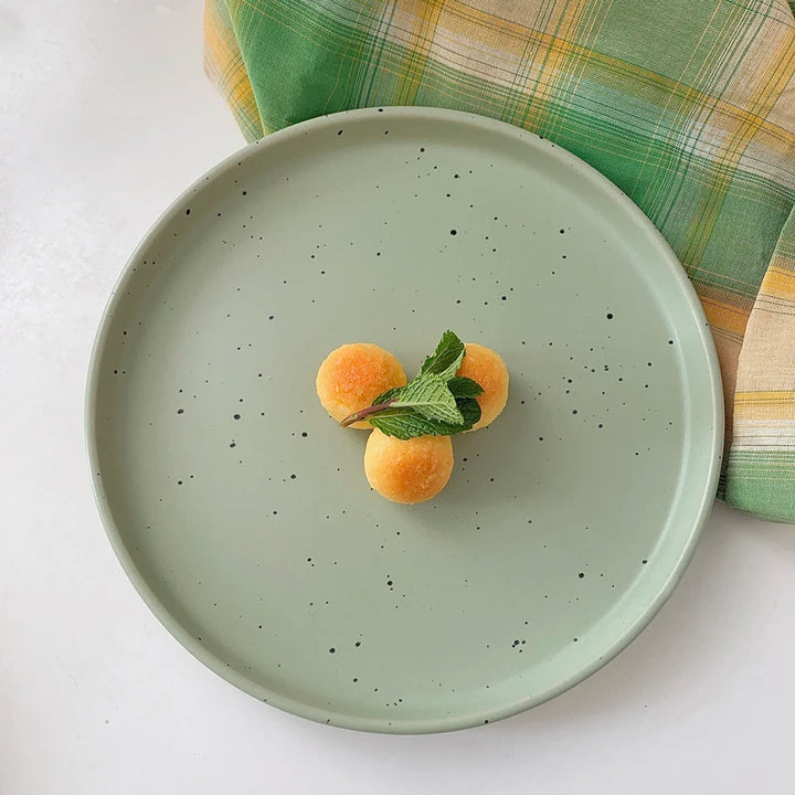 Three minimalist speckled ceramic plates in cream, light grey, and sage green