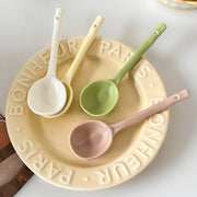 Set of elegant pastel ceramic spoons in green, yellow, white, and pink arranged on a cream-colored plate