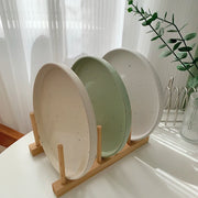 Three minimalist speckled ceramic plates in cream, light grey, and sage green