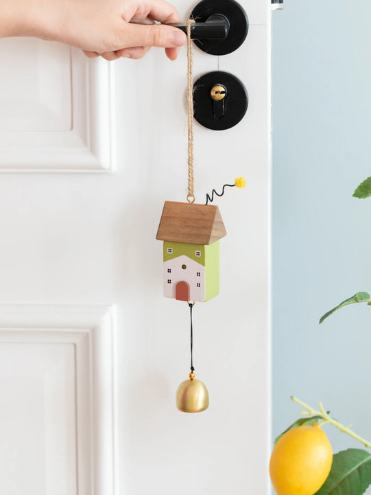 Whimsical wooden house wind chimes with golden bell accents hanging on a rustic frame, perfect for home and garden décor.