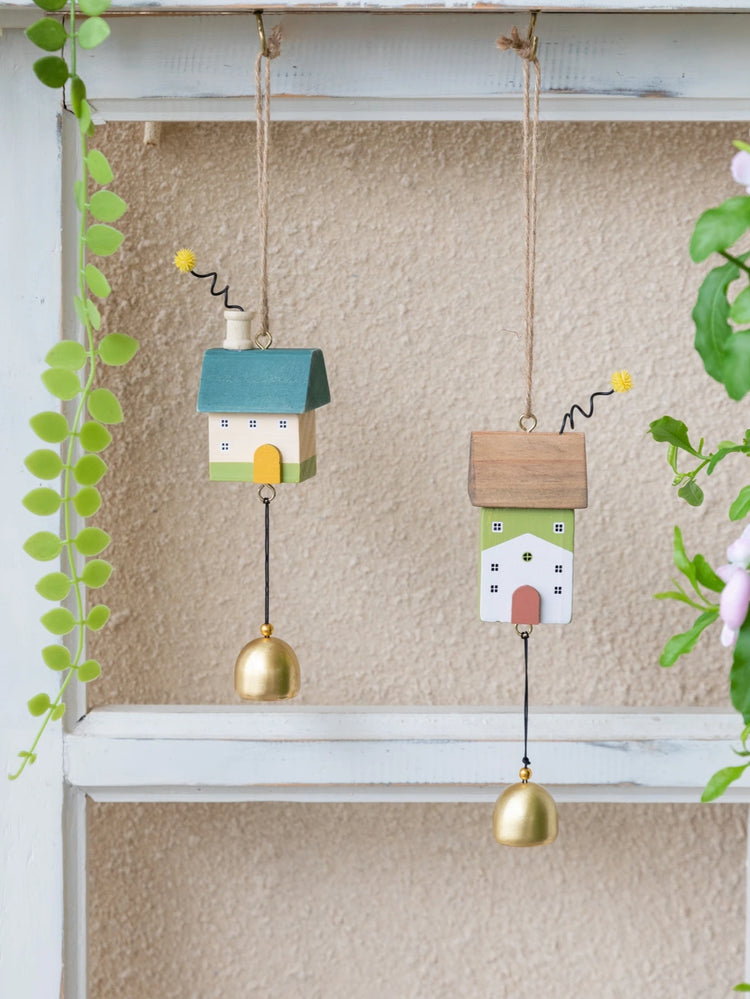 Whimsical wooden house wind chimes with golden bell accents hanging on a rustic frame, perfect for home and garden décor.