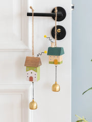 Whimsical wooden house wind chimes with golden bell accents hanging on a rustic frame, perfect for home and garden décor.