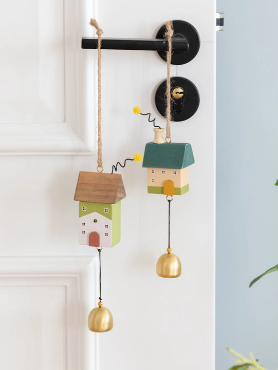 Whimsical wooden house wind chimes with golden bell accents hanging on a rustic frame, perfect for home and garden décor.