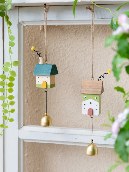 Whimsical wooden house wind chimes with golden bell accents hanging on a rustic frame, perfect for home and garden décor.