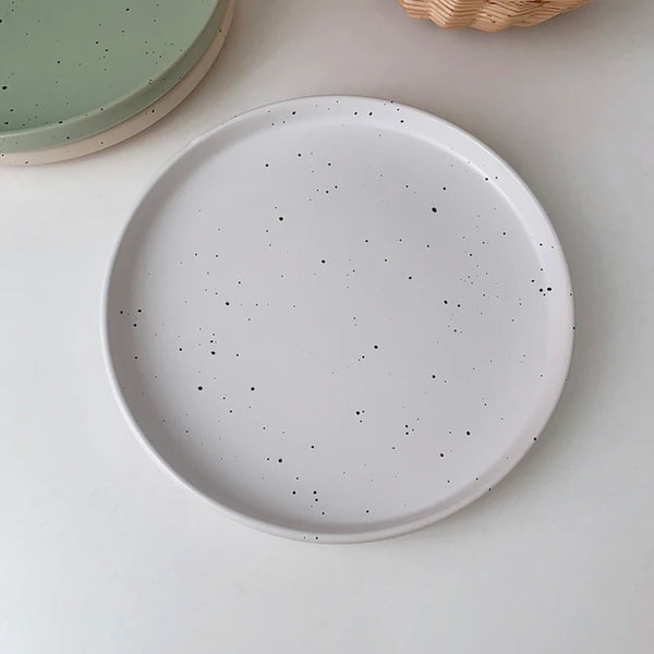 Three minimalist speckled ceramic plates in cream, light grey, and sage green