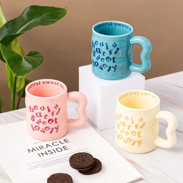 Pink, Yellow, and blue aesthetic wavy ceramic mugs with quirky "beautiful, sweet, lovely" text.
