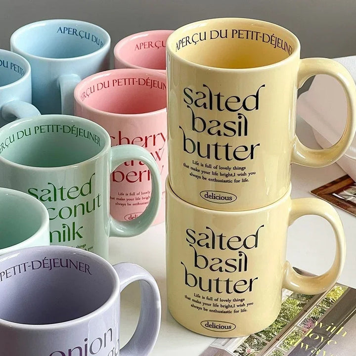 Breakfast-inspired pastel ceramic mugs with playful text designs, featuring unique flavor themes like Salted Basil Butter and Cherry Strawberry, perfect for aesthetic coffee or tea moments